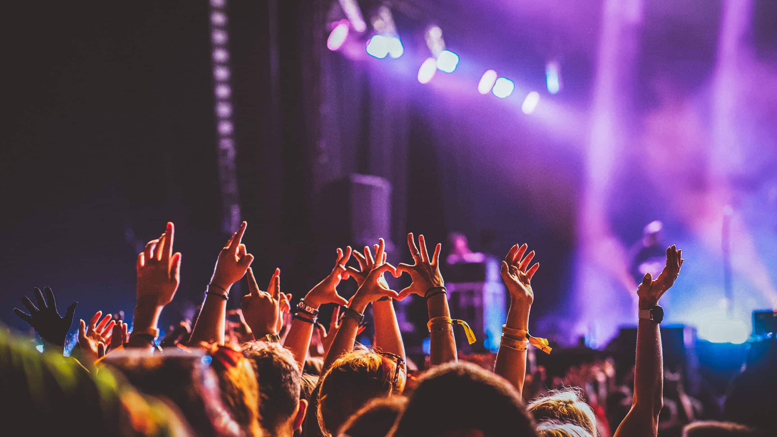 Crowd of people with their hands in the air facing a concert at an event with strobed lights showcasing event and stadium technology